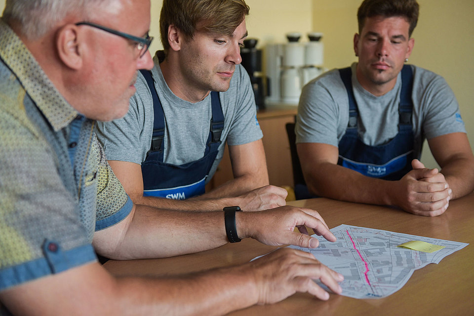 Besprechung SWM Mitarbeiter aus Bereich Abwasser Drei SWM Mitarbeiter aus dem Bereich Abwasser in einer Besprechnung mit einem technischen Plan mit Leitungen