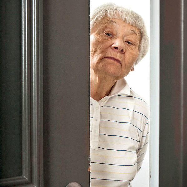 Ältere Dame steht mit skeptischem Blick in offener Haustür. 
