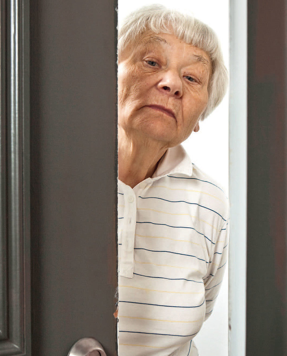 Ältere Dame steht mit skeptischem Blick in offener Haustür. 
