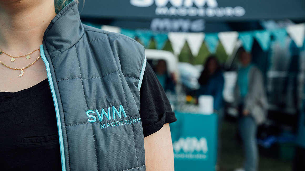 Mitarbeiterin von SWM mit Weste im Vordergrund, SWM Stand im Hintergrund