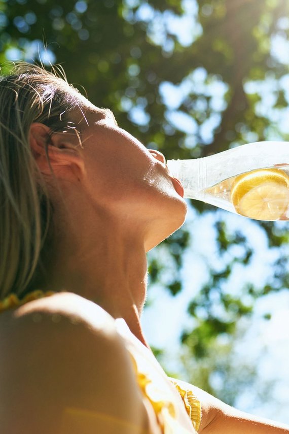 Frau trinkt aus einer Wasserflasche, in der Zitronenscheiben sind