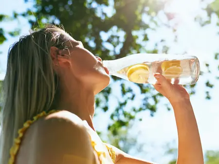 Frau trinkt aus einer Wasserflasche, in der Zitronenscheiben sind