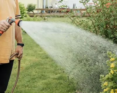 Ein Mann wässert seinen Garten mit einem Gartenschlauch.