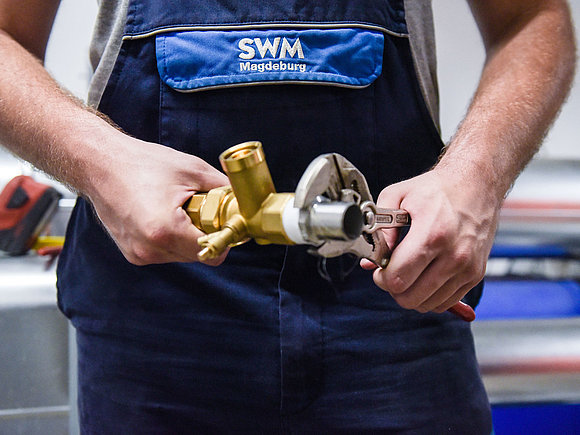 Detailfoto von SWM Azubi zum Anlagenmechaniker mit Rohr und Zange in der Hand