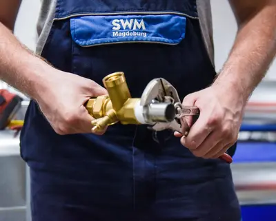 Detailfoto von SWM Azubi zum Anlagenmechaniker mit Rohr und Zange in der Hand