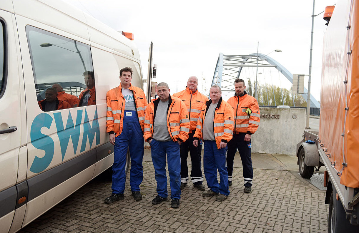 SWM Mitarbeiter Bereich Abwasser stehen in Gruppe zwischen SWM Fahrzeugen