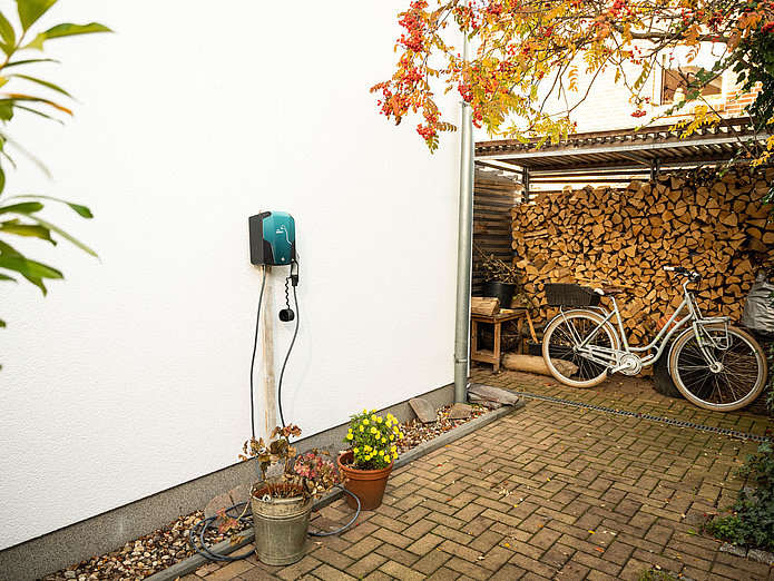 SWM Wallbox an einer Hauswand mit Holzstapel und Fahrrad im Hintergrund