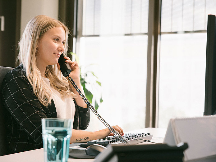 Auszubildende sitzt am PC und telefoniert am Telefon und lacht