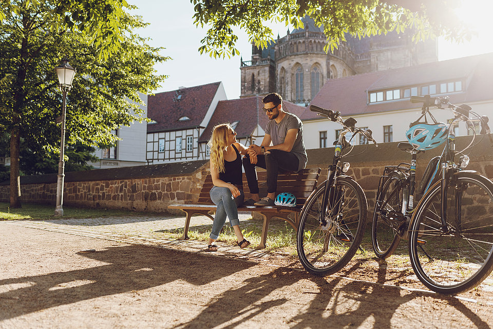 E-Bike Pause am Fürstenwall Ein Pärchen sitzt bei Sonnenschein auf einer Bank am Fürstenwall in Magdeburg, neben Ihnen stehen zwei SWM-E-Bikes.