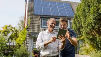 Zwei Männer stehen mit einem Tablet vor einem Haus mit Solardach