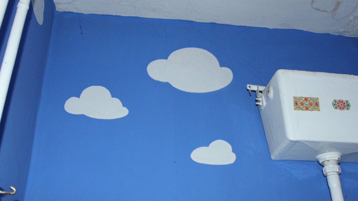 Blau gestrichene Wand mit weißen Wolken und altem Toilettenspülkasten