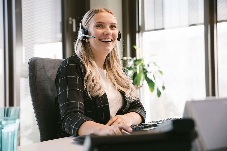 Auszubildende sitzt mit Headset am PC und lacht