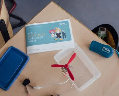 BlitzKitz-Forscherbuch und verschiedene Bestandteile zum Experimentieren liegen auf einem Schultisch
