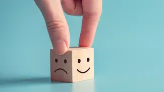 Finger halten einen Holzwürfel mit zwei Gesichtern, ein zufriedenes und ein Unzufriedenes Lächeln