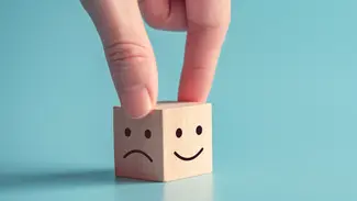Finger halten einen Holzwürfel mit zwei Gesichtern, ein zufriedenes und ein Unzufriedenes Lächeln
