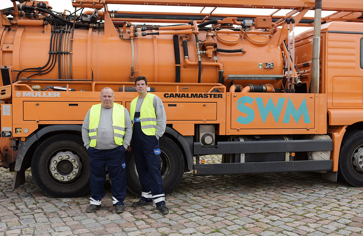 Zwei SWM Mitarbeiter der Abwasserentsorgung stehen vor einem Kanalspülfahrzeug