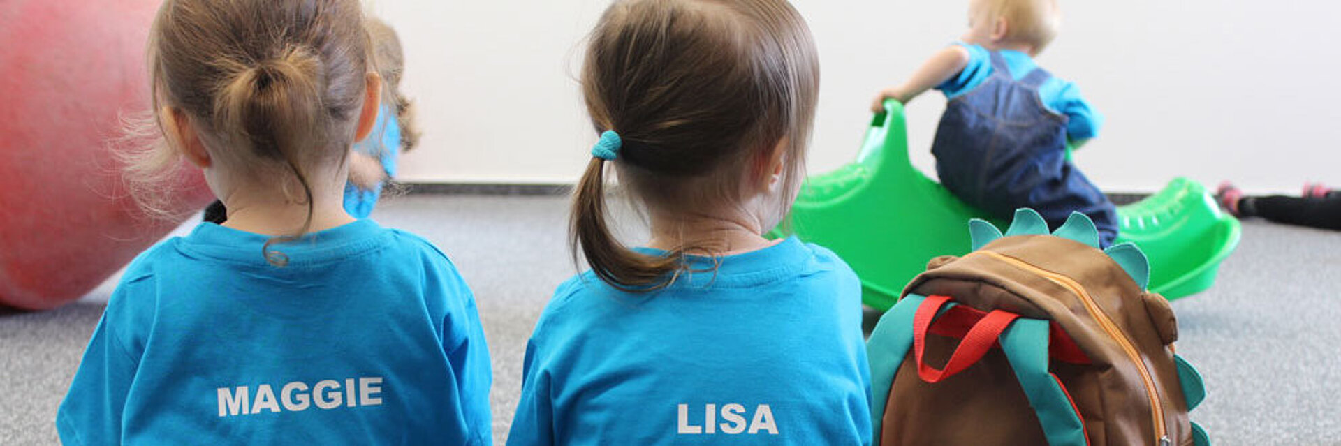 Zwei Kinder im SWM T-Shirt sitzen mit dem Rücken zur Kamera in der SWM Kita