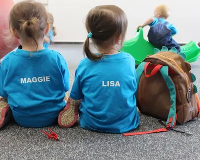 Zwei Kinder im SWM T-Shirt sitzen mit dem Rücken zur Kamera in der SWM Kita