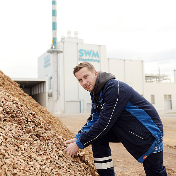 SWM Mitarbeiter greift in einen großen Berg Holzhackschnitzel vor dem SWM Biomasseheizkraftwerk.