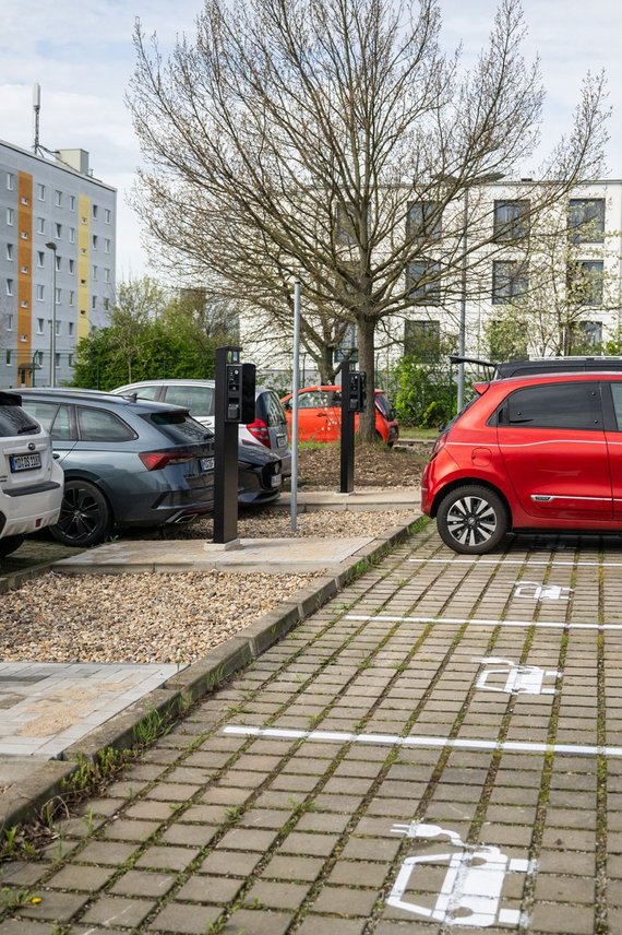 Blick auf einen Parkplatz mit E-Ladesäulen und einer Ladesäule tankt ein rotes Auto