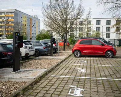 Blick auf einen Parkplatz mit E-Ladesäulen und einer Ladesäule tankt ein rotes Auto