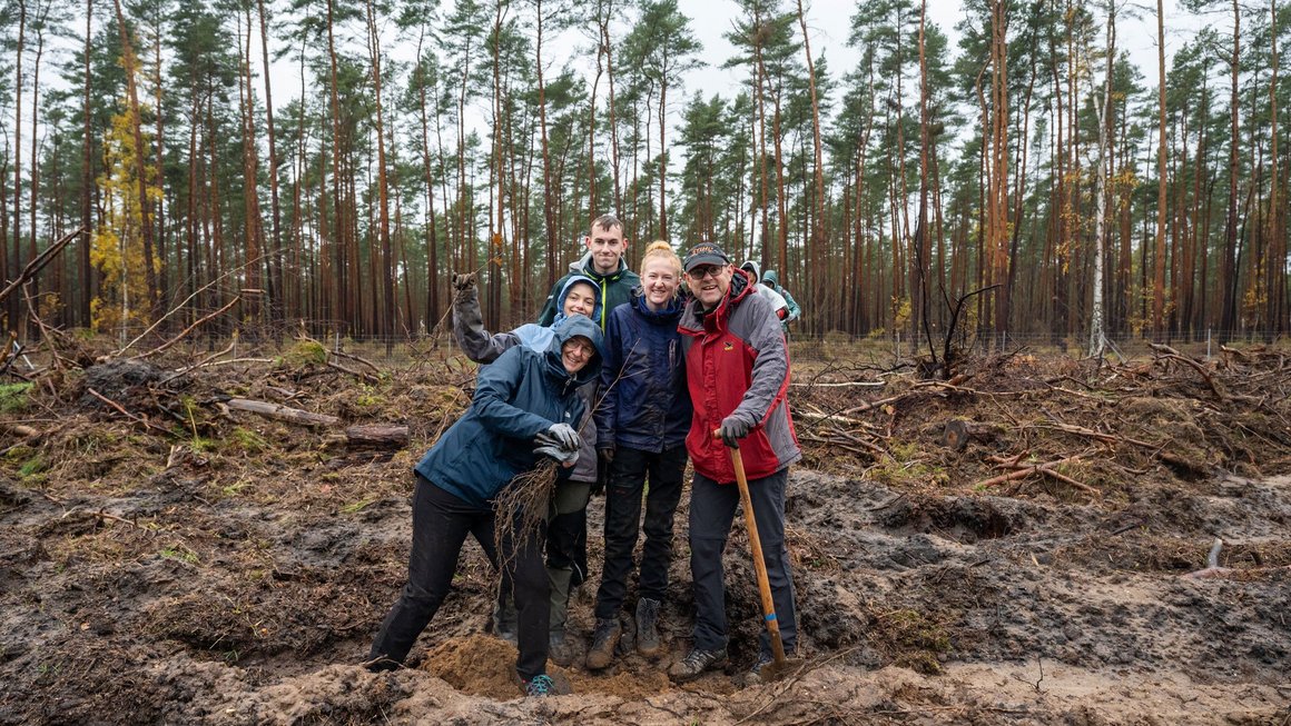 Familie beim Baumpflanzen in Gruppe zusammen und lachen in die Kamera