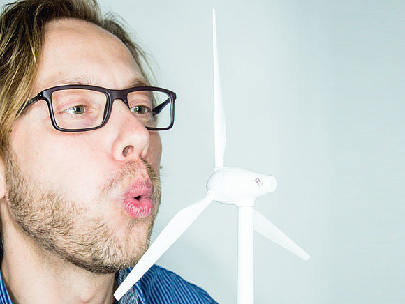 Windkraft SWM Mitarbeiter pustet auf ein kleines Windrad